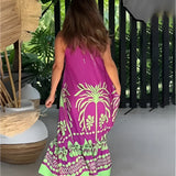 Tropical maxi dress with a vibrant purple and green palm design, featuring loose sleeves and a flowing silhouette. The dress is being worn outdoors near a fence, surrounded by greenery and grass, showcasing a colorful pattern with tints and shades of magenta.
