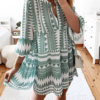 Tropical Print Button-Up Mini Dress in light green with pink accents, modeled by a person wearing the dress. The dress features short sleeves and a mini length, highlighting a vibrant summer style. The model's arms and legs are visible, emphasizing the dress's fit and style.