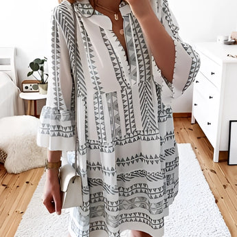 A person wearing a gray tropical print button-up mini dress with a summery design, styled with short sleeves and a collar, standing with their hand on their hip.