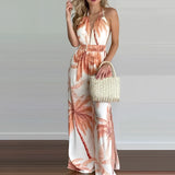 A model wearing a tropical print halter maxi dress suitable for beach weddings and resort wear, accessorized with sunglasses and a bag, highlighting the dress's flowing design that fits comfortably around the waist and falls elegantly to the thighs and knees.