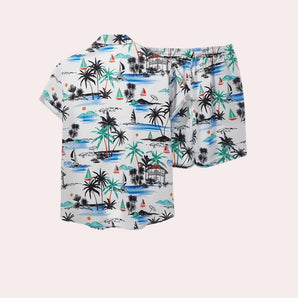 Tropical print shirt and shorts set featuring a palm tree and beach scene design with aqua accents, suitable for baby and toddler clothing. The shirt has a collar and short sleeves, while the matching shorts have a relaxed fit.