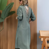 Turquoise linen summer dress with an asymmetrical hem, featuring long sleeves and a round neckline. The dress has a fitted waist and reaches the knee, showcasing a fashionable design.
