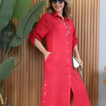 Woman wearing a turquoise linen asymmetrical hem long sleeve summer dress, accessorized with sunglasses, highlighting the sleeves and waist.