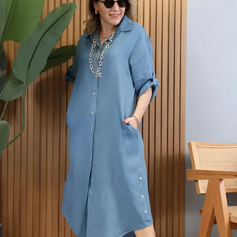 Turquoise linen summer dress with asymmetrical hem and long sleeves worn by a person standing, showcasing the dress's elegant design and vibrant azure color.