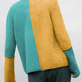Unisex eco-friendly knit sweater made from handmade wool, featuring a two-tone design in green and blue, displayed on a mannequin showcasing the joint, arm, and shoulder areas.