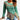 Mint green and brown asymmetrical ruffled sweater with toggle, featuring a unique two-tone design. The sweater highlights shoulder detailing, a stylish neckline, and sleek long sleeves. It is tailored for an XL fit, accentuating the waist and extending to the thigh. The textile has a textured appearance, enhancing the overall fashionable outerwear look.