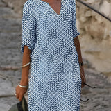 Woman wearing a blue and white V-neck geometric print loose fit summer dress with 3/4 sleeves, posing with her arms slightly bent.