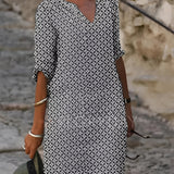 A woman wearing a green and white V-neck geometric print loose fit summer dress with 3/4 sleeves, standing and looking sideways, with her hand on her hip.