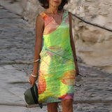 Woman wearing a green sleeveless summer dress with a vibrant leaf pattern, showcasing her shoulders and legs.
