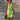 Woman wearing a green sleeveless summer dress with a vibrant leaf pattern, showcasing her shoulders and legs.