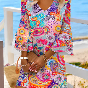 Vibrant paisley bohemian V-neck mini dress in multicolor, featuring an array of green and orange patterns, displayed on a mannequin against a white background.