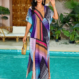 A woman wearing a vibrant print kaftan dress, standing near water with tropical plants in the background, smiling and enjoying a sunny day.