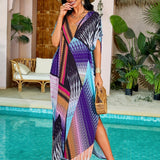 Woman wearing a vibrant print kaftan standing by the water, showcasing a luxury resort and tropical beach dress with green and azure patterns, featuring a relaxed fit with wide sleeves and a flowing waist.