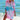 Woman wearing a vibrant tie-dye beach cover-up dress in pink mermaid design, standing by the water, looking happy and relaxed, showcasing summer beachwear fashion.