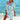 Colorful boho tunic dress in a vibrant blue coral tie-dye pattern, being worn as a beach cover-up. The dress features a relaxed fit with sleeves, a round neckline, and falls loosely around the waist. It is styled in an outdoor setting on the beach, evoking a happy and carefree vibe.