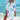 Woman wearing a vibrant tie-dye beach cover-up dress in blue seahorse pattern, standing on the beach with water in the background, smiling and enjoying the summer.