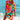 Colorful boho tunic dress with vibrant orange and pink tie-dye patterns, featuring a loose fit and flowy sleeves, worn by a person enjoying a sunny day by the water.