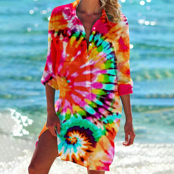 Colorful boho tunic dress with vibrant orange and pink tie-dye patterns, featuring a loose fit and flowy sleeves, worn by a person enjoying a sunny day by the water.
