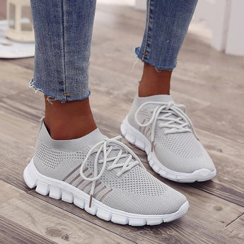 Gray women's lightweight neon running shoes displayed on a model's feet, showcasing the breathable and fashionable design ideal for sportswear. The shoes have a blend of gray and black tones, with the model standing on a neutral background.