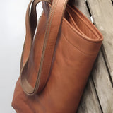Vintage brown distressed leather tote handcrafted luxury bag with sturdy handles, suitable for travel and daily use, placed on a wooden surface.