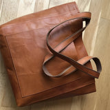 Vintage brown distressed leather tote handcrafted luxury bag with sturdy handles, displayed on a wooden surface.