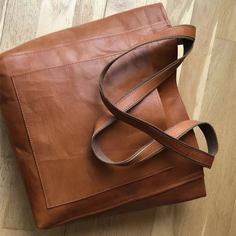 Vintage brown distressed leather tote handcrafted luxury bag with sturdy handles, displayed on a wooden surface.