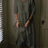 Woman wearing a dark green, loose-fitting vintage linen dress with short sleeves, standing near a window with blinds. The dress features a bohemian style, perfect for summer, and is in a size 5XL.