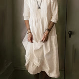Vintage white linen dress in a bohemian loose fit, featuring a lightweight design perfect for summer. The image showcases the dress on a model, highlighting its long sleeves, collared neckline, and defined waist. The model's hand gesture and relaxed pose emphasize the dress's airy and comfortable style.