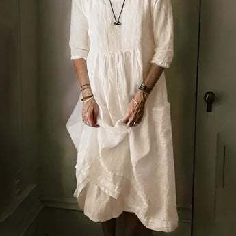 Vintage white linen dress in a bohemian loose fit, featuring a lightweight design perfect for summer. The image showcases the dress on a model, highlighting its long sleeves, collared neckline, and defined waist. The model's hand gesture and relaxed pose emphasize the dress's airy and comfortable style.