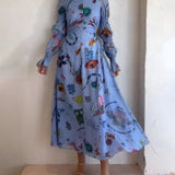 Whimsical blue maxi dress featuring colorful embroidery and intricate patterns, with a flowing design and long sleeves.