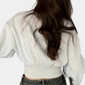 Cropped white cable knit sweater with long sleeves, showcasing a classic knit pattern and a cozy, fashionable design.