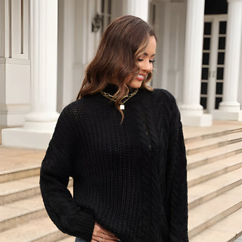 
A woman wearing a white cable knit turtleneck sweater paired with jeans, showcasing a cozy winter fashion look. The sweater features a high collar and long sleeves, perfect for keeping warm in colder weather.