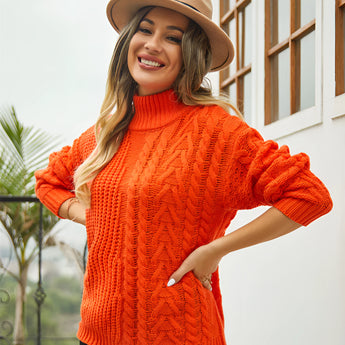 
A woman wearing an orange cable knit turtleneck sweater stands next to a window. She is smiling and accessorized with sunglasses and a hat, showcasing a cozy winter fashion style in an XL size.
