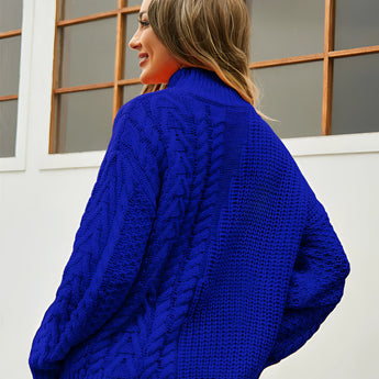 A woman wearing a white cable knit turtleneck sweater with long sleeves, smiling and standing near a window. The cozy winter garment features a textured pattern and a high collar, ideal for cold weather fashion.