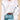 White cross-stitch V-neck sweater with bow-knot detailing, featuring long sleeves and a fitted waist, worn by a woman.