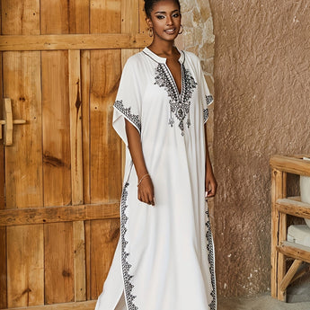 White Embroidered Bohemian Kaftan with V-Neck, Moroccan Resort Dress featuring detailed embroidery, hanging on a door.