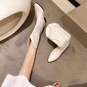 White embroidered women's western cowboy boots on a wooden floor, showcasing intricate design and stylish craftsmanship.