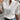A woman wearing a white floral embroidered lace blouse with sheer fabric, paired with jeans. The blouse features short sleeves and intricate detailing around the neck and chest area.