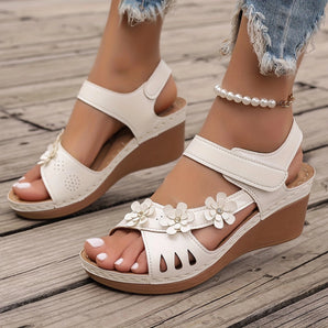 White floral wedge sandals featuring a beaded strap, cutout design, and wedge heel, showcased on a model's foot against a neutral background.