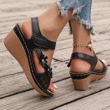 White floral wedge sandals with a beaded strap and cutout design being worn on a model's foot, showcasing the intricate detailing and stylish design.