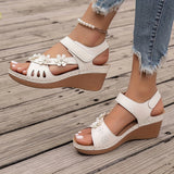 White floral wedge sandals featuring a beaded strap and cutout design, worn on a person's foot.