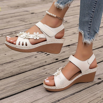 White floral wedge sandals featuring a beaded strap and cutout design, worn on a person's foot.