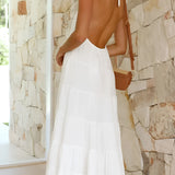 White halterneck tiered midi dress displayed on a model, showcasing its elegant design suitable for summer resort wear, with a focus on the dress's flowing silhouette and stylish halterneck neckline.