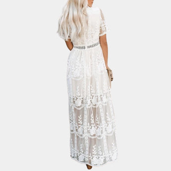 White lace maxi dress with a bohemian v-neck design, featuring delicate embellishments and long flowing sleeves, ideal for a beach wedding.