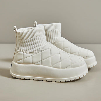 White quilted insulated lightweight winter snow boots displayed on a beige couch, highlighting their comfort and stylish design.