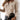 
A woman wearing a white ribbed henley blouse with fitted long sleeves, styled as a dress shirt. The blouse is paired with black pants and is showcased in a beige color, size XL. The image focuses on the upper body, highlighting the shoulder, arm, and hand details of the blouse.
