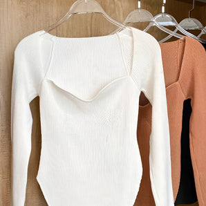 White ribbed scoop neck long sleeve bodysuit on a clothes hanger, showcasing the stylish neckline and sleeve design against a neutral background.