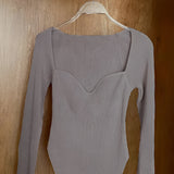 
Gray ribbed scoop neck long sleeve bodysuit on clothes hanger, showcasing neckline and sleeve design.