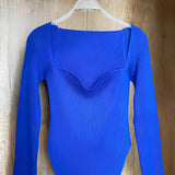 White ribbed scoop neck long sleeve bodysuit for women in XL, displayed on a clothes hanger against a grey background. The garment is a one-piece fashion top with a simple and chic design suitable for casual or formal wear.
