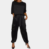 
A woman wearing a black satin jumpsuit with cargo pants, featuring long sleeves and a tailored waist, suitable for loungewear or casual outings.